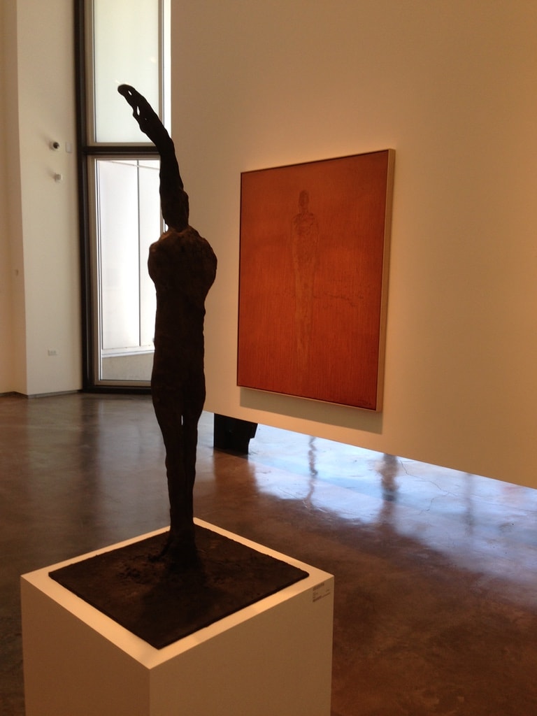 LewAllen Gallery — bronze figure sculpture with arm raised beside large orange canvas
